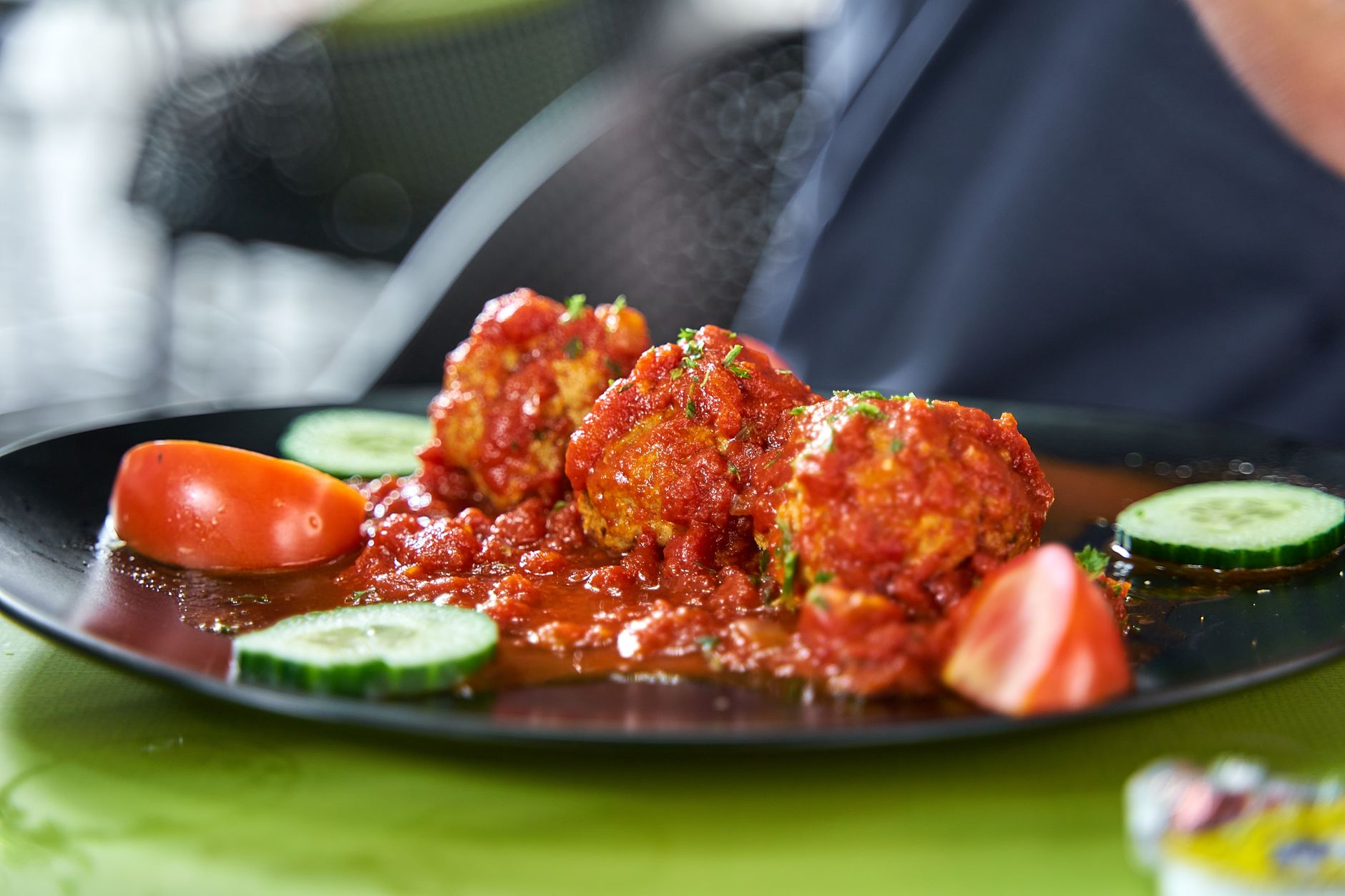 Plate of flavorful meatballs in rich tomato sauce garnished with cucumber and tomato slices.