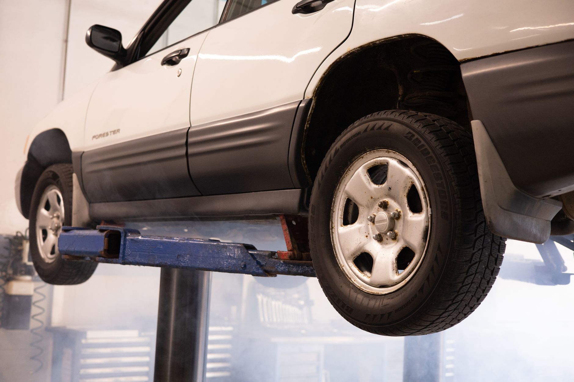 A white car suspended on a lift in an automotive repair shop, showcasing maintenance work.
